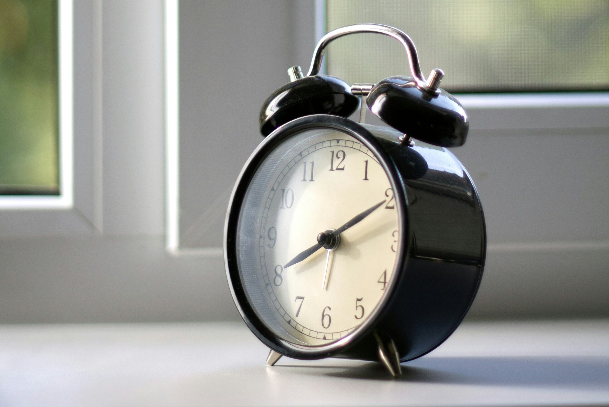 Vintage black alarm clock sitting on a windowsill with soft morning light shining through, symbolizing quiet reflection and the passage of time.