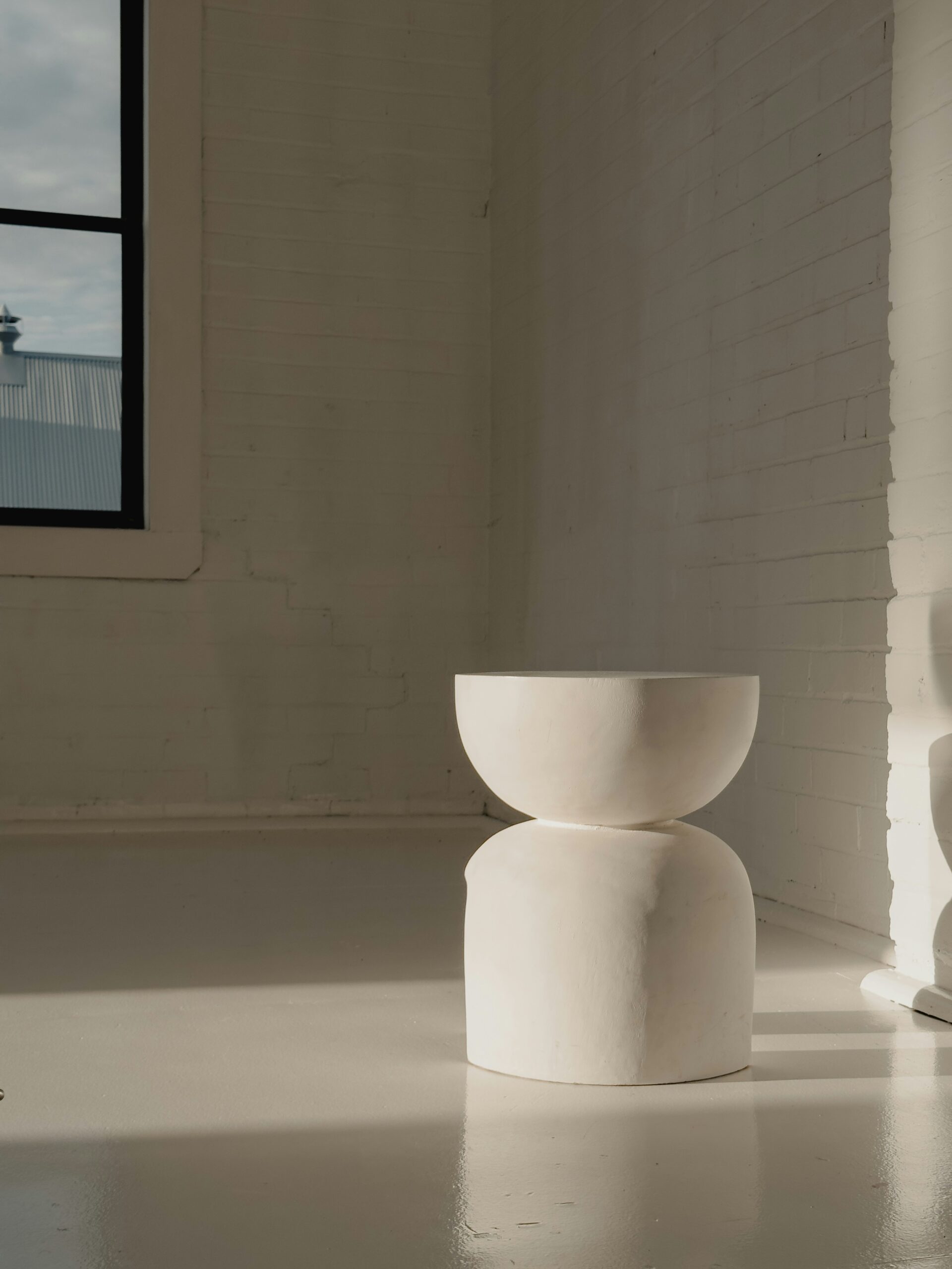 Minimalist white ceramic stool in sunlit studio corner with modern aesthetic symbolizing embracing new wineskins