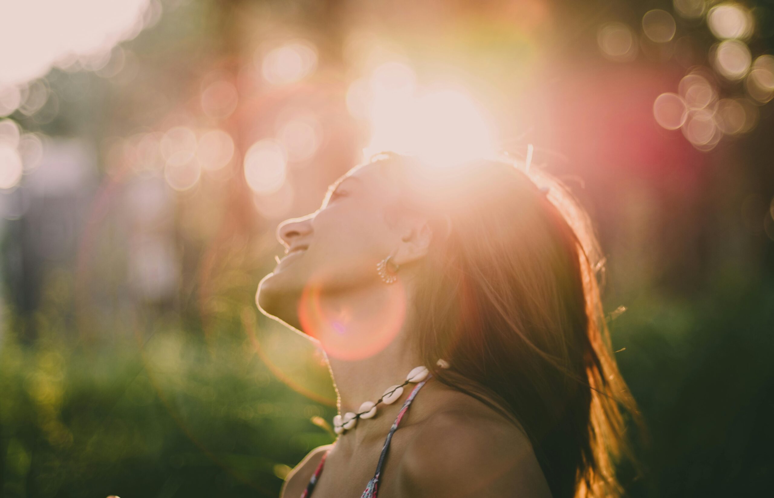Woman basking in warm sunlight, eyes closed and smiling peacefully in nature
